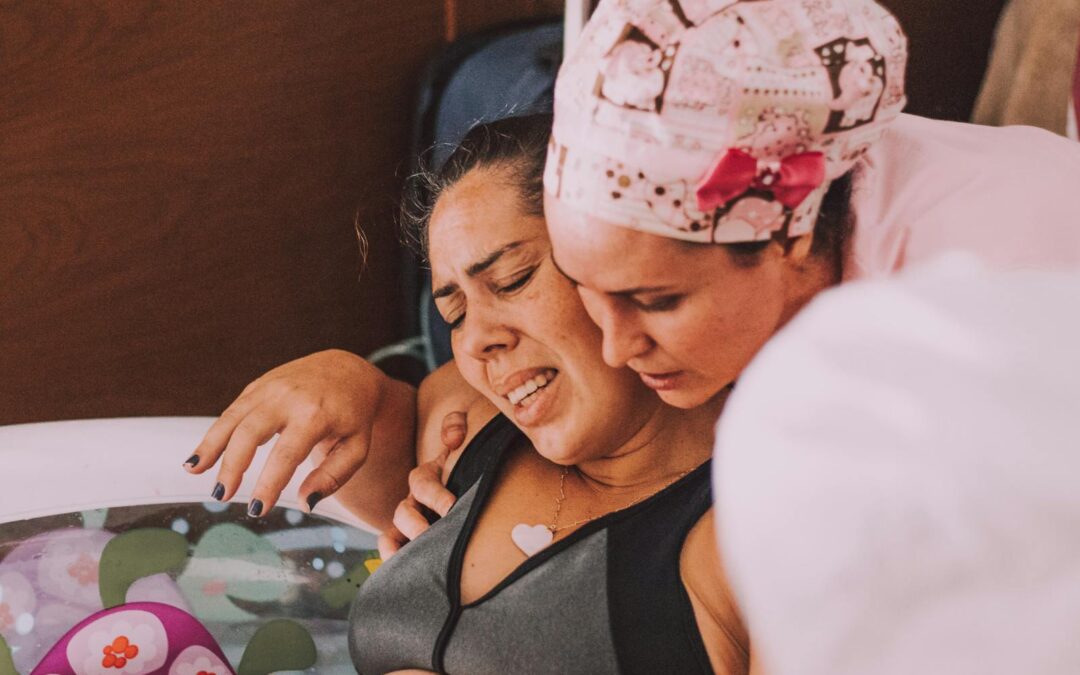 A midwife comforts a pregnant woman during a water birth at home.