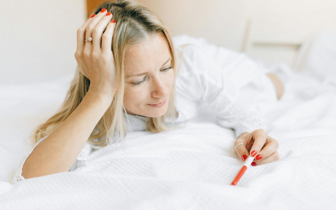 A woman lying on a bed looks at a pregnancy test, expressing contemplation and emotion.
